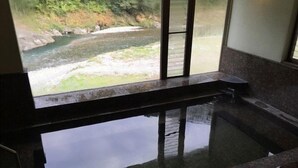 Un área de spa con un amplio ventanal que da a un paisaje natural, una bañera de piedra y un pequeño rincón de descanso.