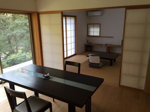 A traditional Japanese-style room with tatami flooring, a low table with chairs, a sliding shoji screen, and a view of greenery outside. - Matsuno Onsen Suikoen (Okutama)