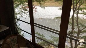 Habitación con un ventanal grande que da a un río y árboles. Se observa una silla de madera con un cojín estampado.
