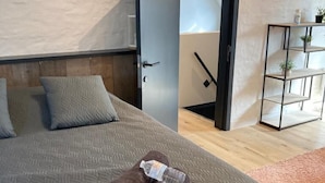 Un dormitorio con cama, almohadas, una toalla, una puerta, una estantería con plantas y una escalera.
