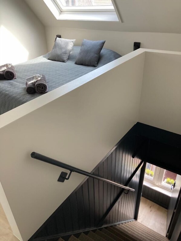 A modern loft bedroom with a skylight, a bed with rolled towels, and a staircase with a handrail.