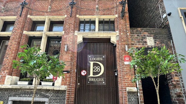 Un edificio de ladrillo con una puerta de madera grande, identificada con la señal “Logies 28 Bruges”.