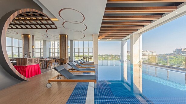A modern indoor pool area with lounge chairs, a bar, and large windows offering a city view. - Jasmine Palace Hotel (Yangon)