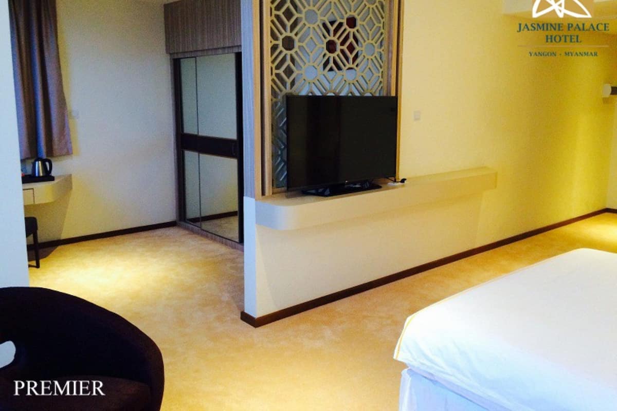 A hotel room with a bed, a TV mounted on the wall, a small table with a kettle, and a decorative screen.