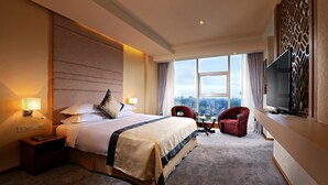 A hotel room with a large bed, a TV, a desk, and a view of the city. - Jasmine Palace Hotel (Yangon)