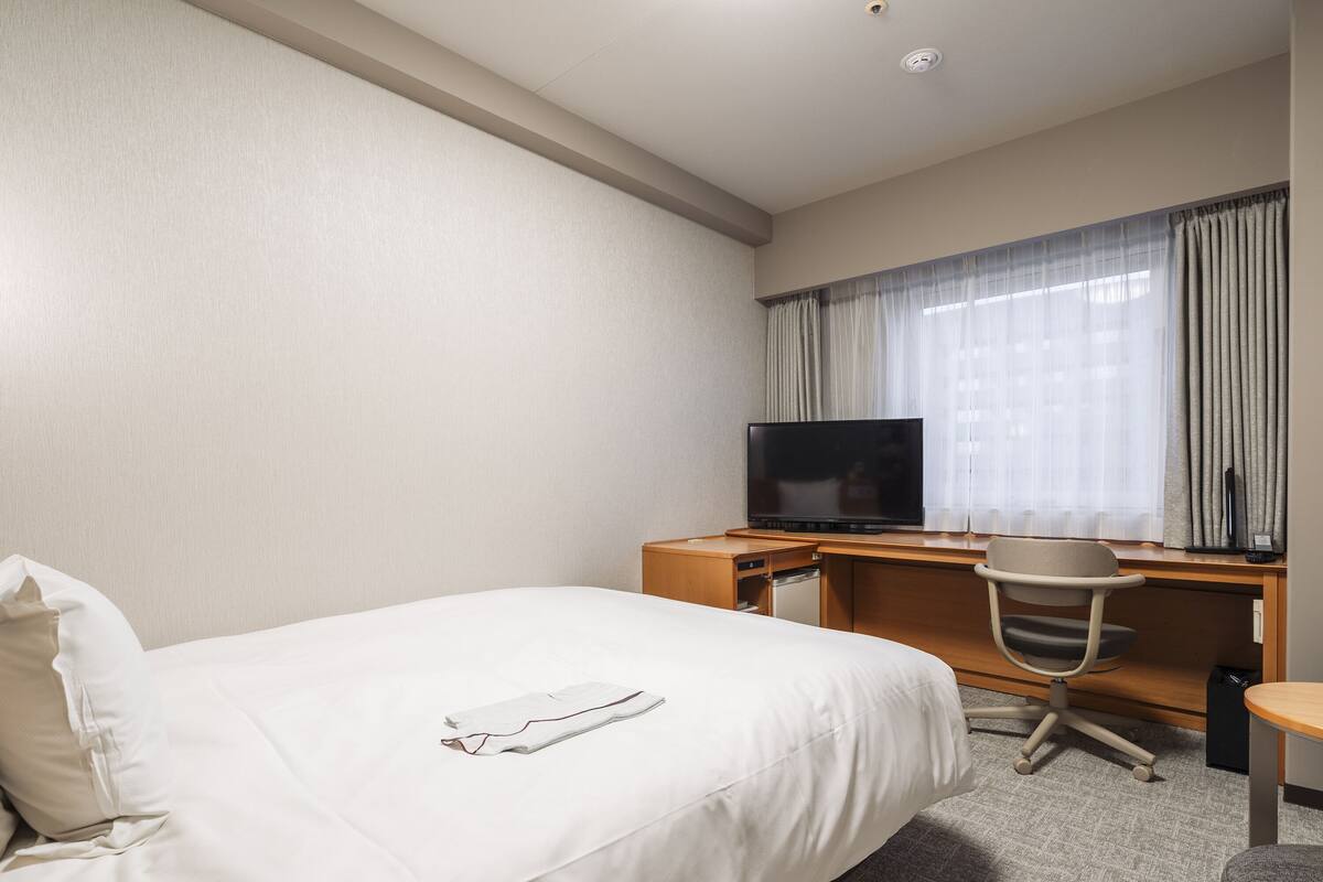 A hotel room with a bed, a desk, a chair, a television, and a window with curtains.