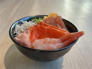 Un tazón de sashimi con camarones y salmón, adornado con wasabi verde y jengibre encurtido.