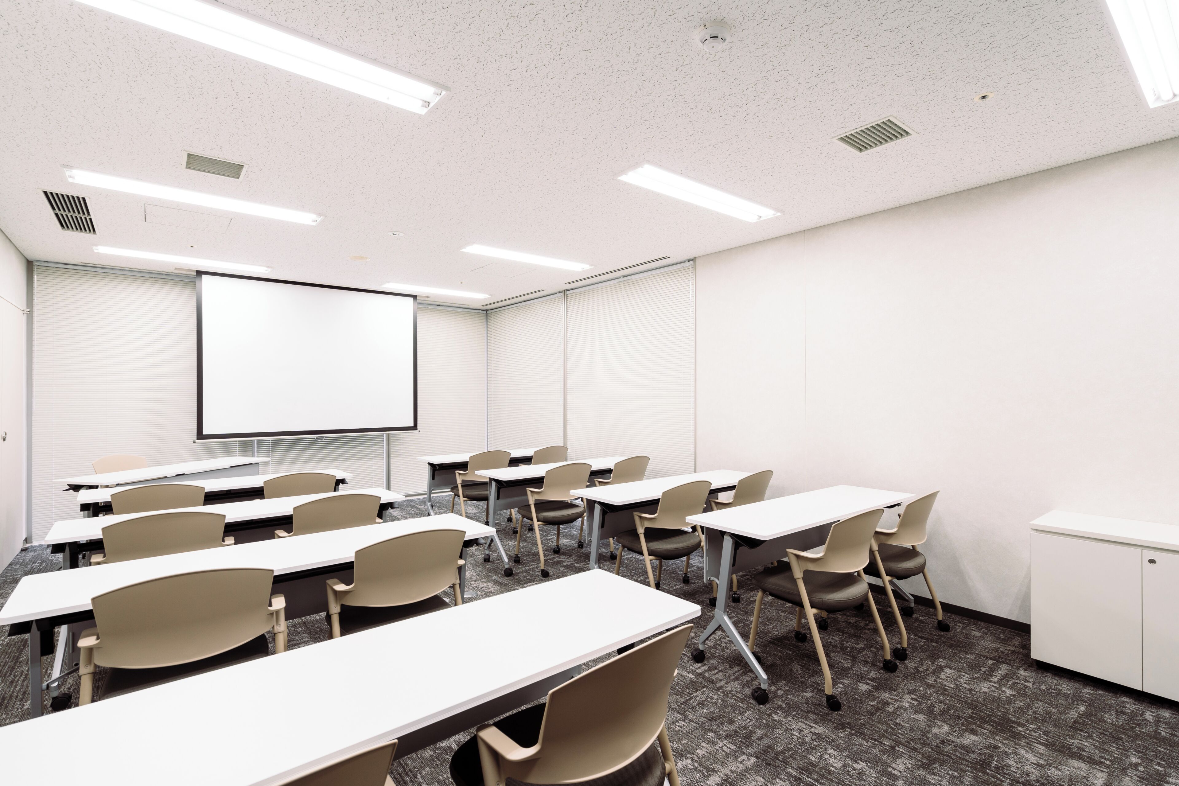 A conference room with white tables, chairs, a projector screen, and a whiteboard.