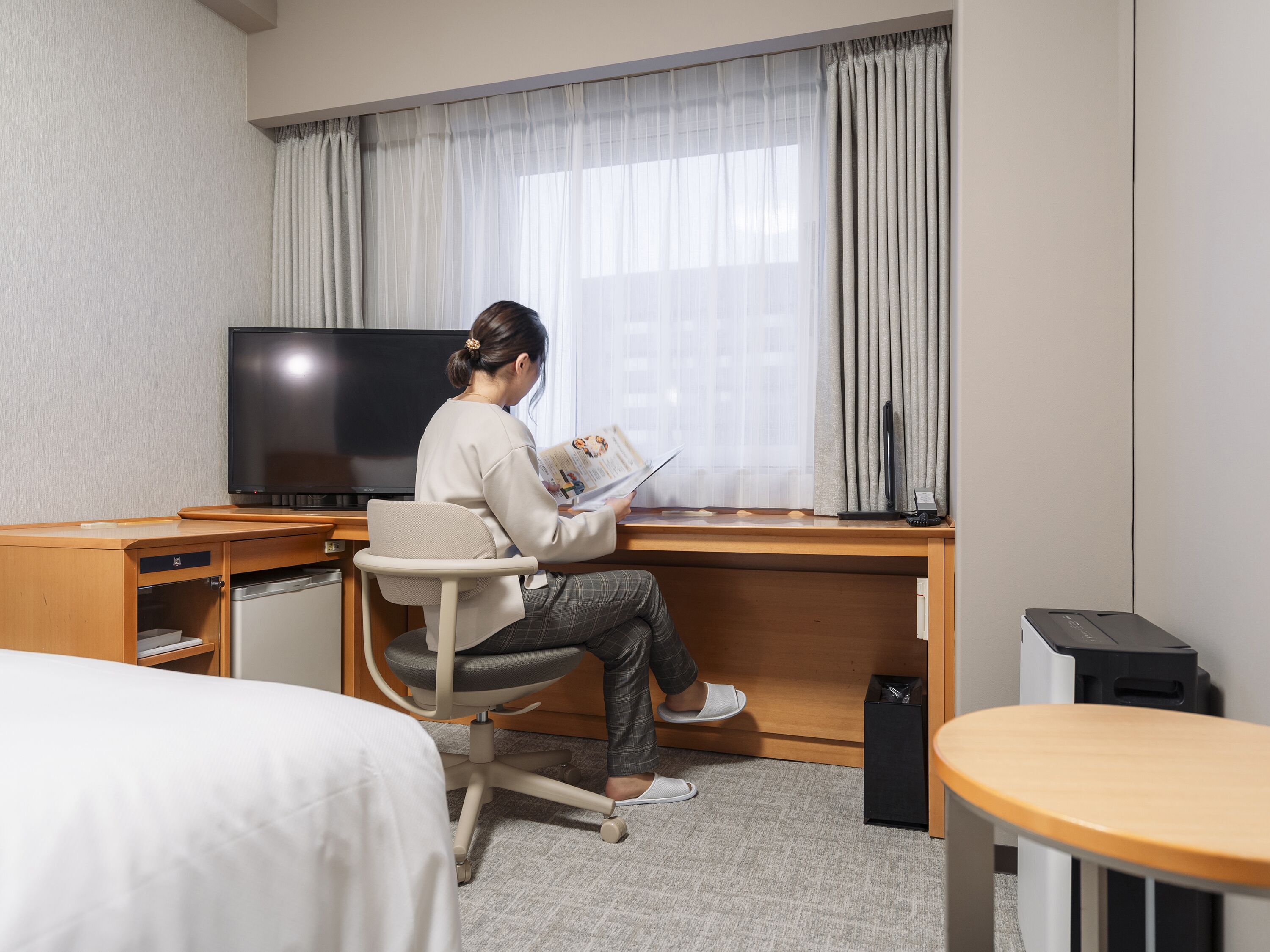 Een hotelkamer met een bed, een bureau met computer, een televisie en een raam met gordijnen.