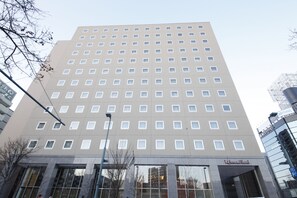 Un hotel alto de diseño moderno, con una fachada de ventanas enrejada y una entrada destacada que muestra el nombre del hotel.