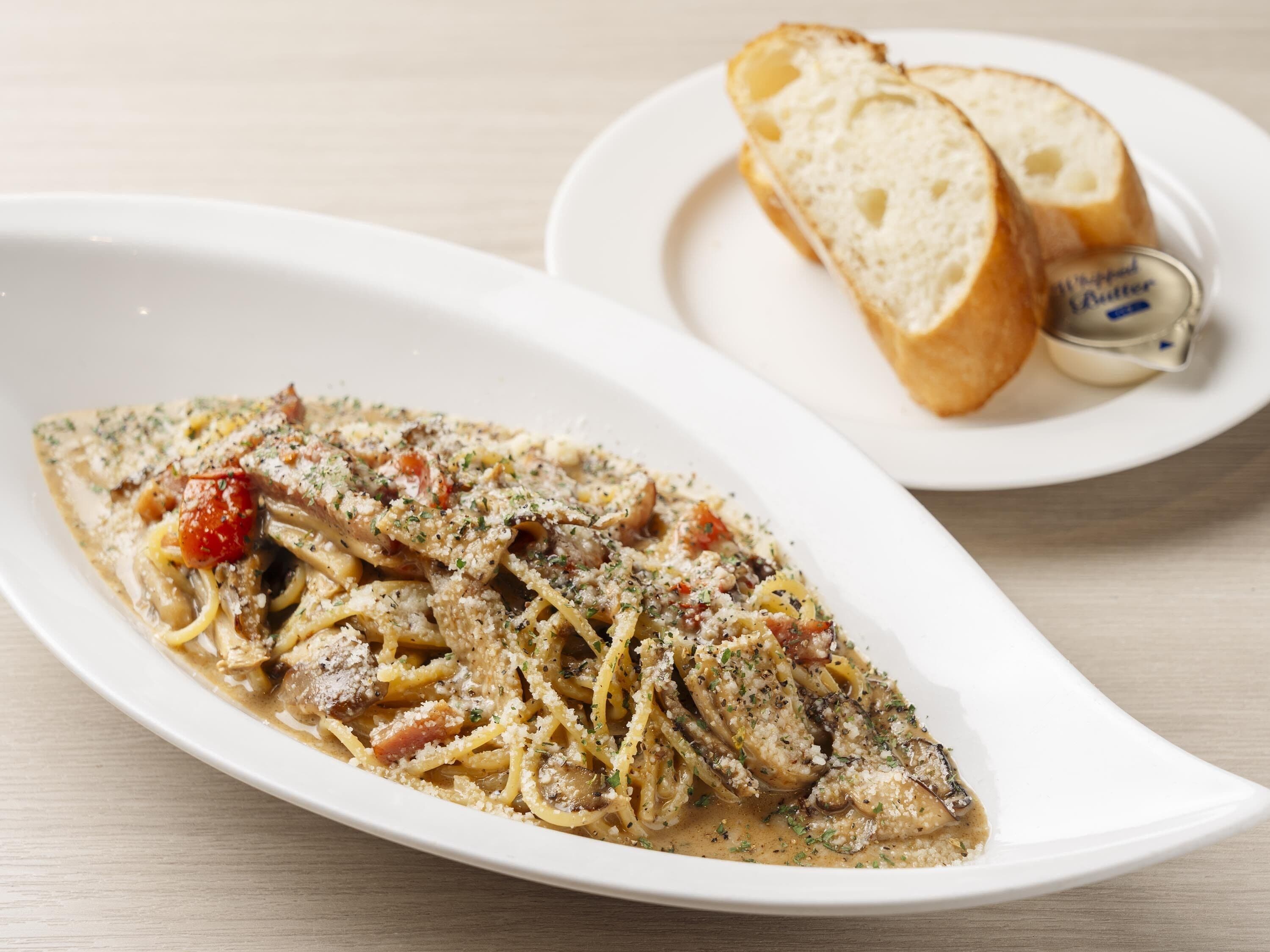 A plate of spaghetti with a creamy sauce, garnished with herbs and cheese, and a side of bread and butter.