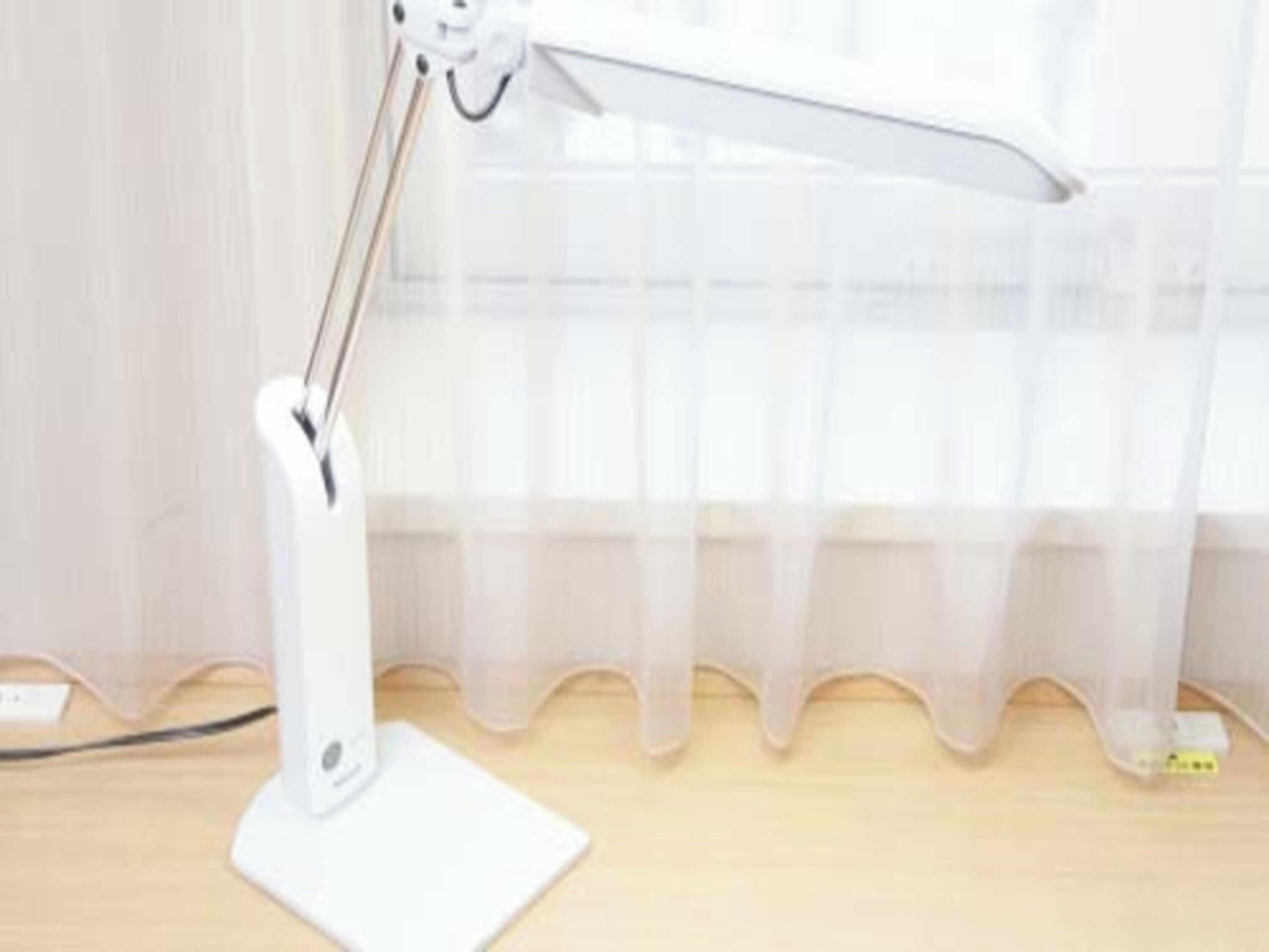 A white desk lamp with a flexible neck on a wooden desk.