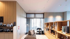 A modern hotel room with a wooden wardrobe, a sofa, a bookshelf, and a window with blinds.
