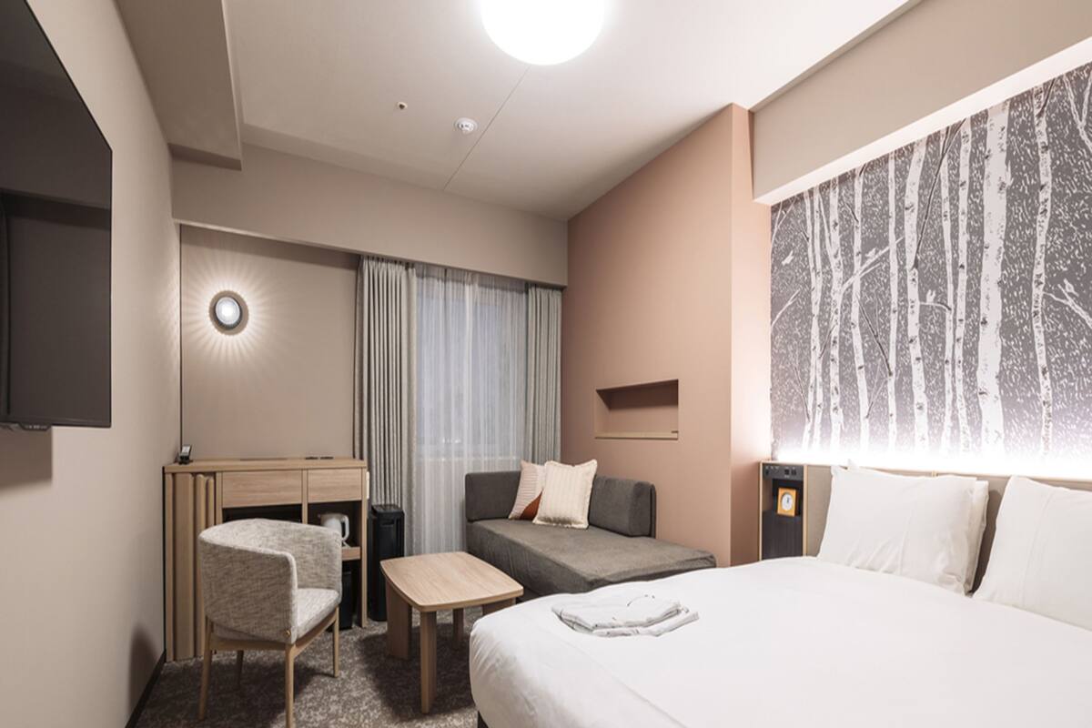 A hotel room with a bed, a desk, a chair, a small table, and a TV.