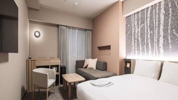 Hotellihuone, jossa on sänky, työpöytä, tuoli, pieni pöytä ja televisio.