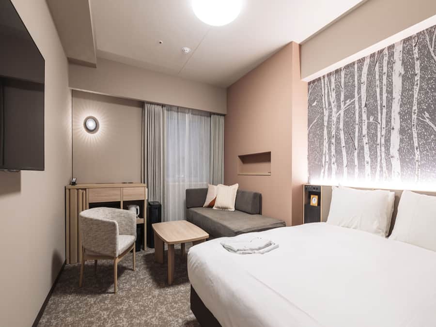 Ein Hotelzimmer mit Bett, Schreibtisch, Stuhl, Nachttisch und Fernseher.