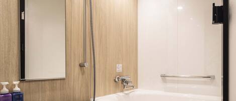 A modern bathroom with a bathtub, a shower with a handheld hose, and a mirror. There are toiletries on the counter.