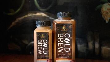 Two bottles of Arenal Cold Brew coffee on a wooden surface with scattered coffee beans.