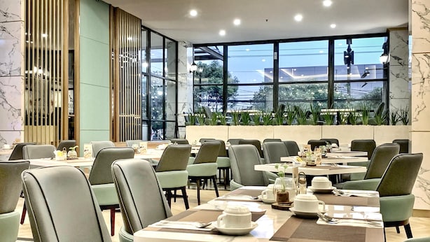 A modern dining area with multiple tables and chairs, large windows with a view of greenery, and a clean, contemporary design. - Grand Kangen Hotel Urip Sumoharjo Yogyakarta (Yogyakarta)
