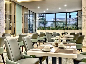 Uma sala de jantar moderna com várias mesas e cadeiras, janelas amplas com vista para o verde e um design limpo e contemporâneo.
