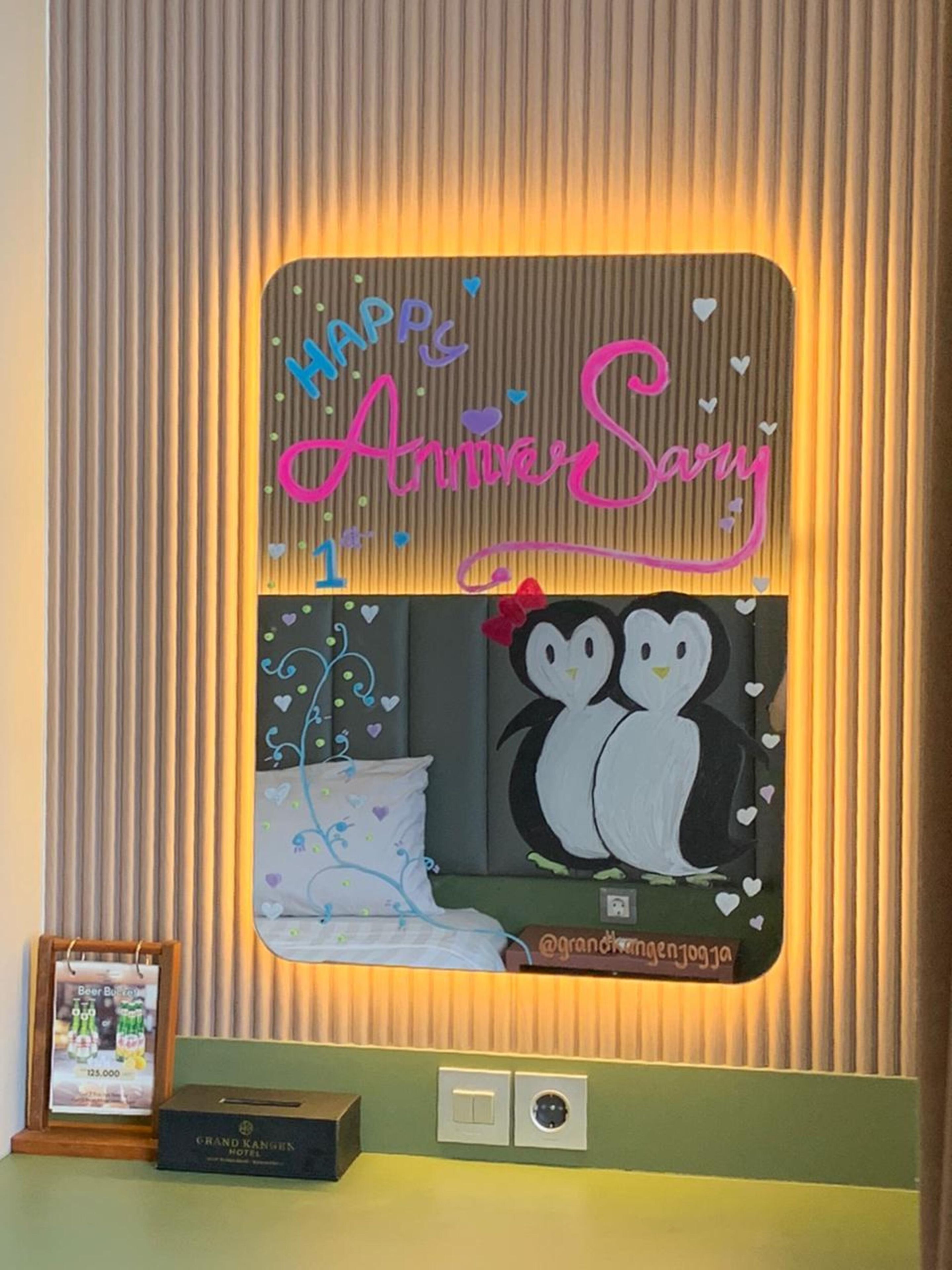 A hotel room with a mirror reflecting a bed, a pillow, and a wall with a decorative sign.