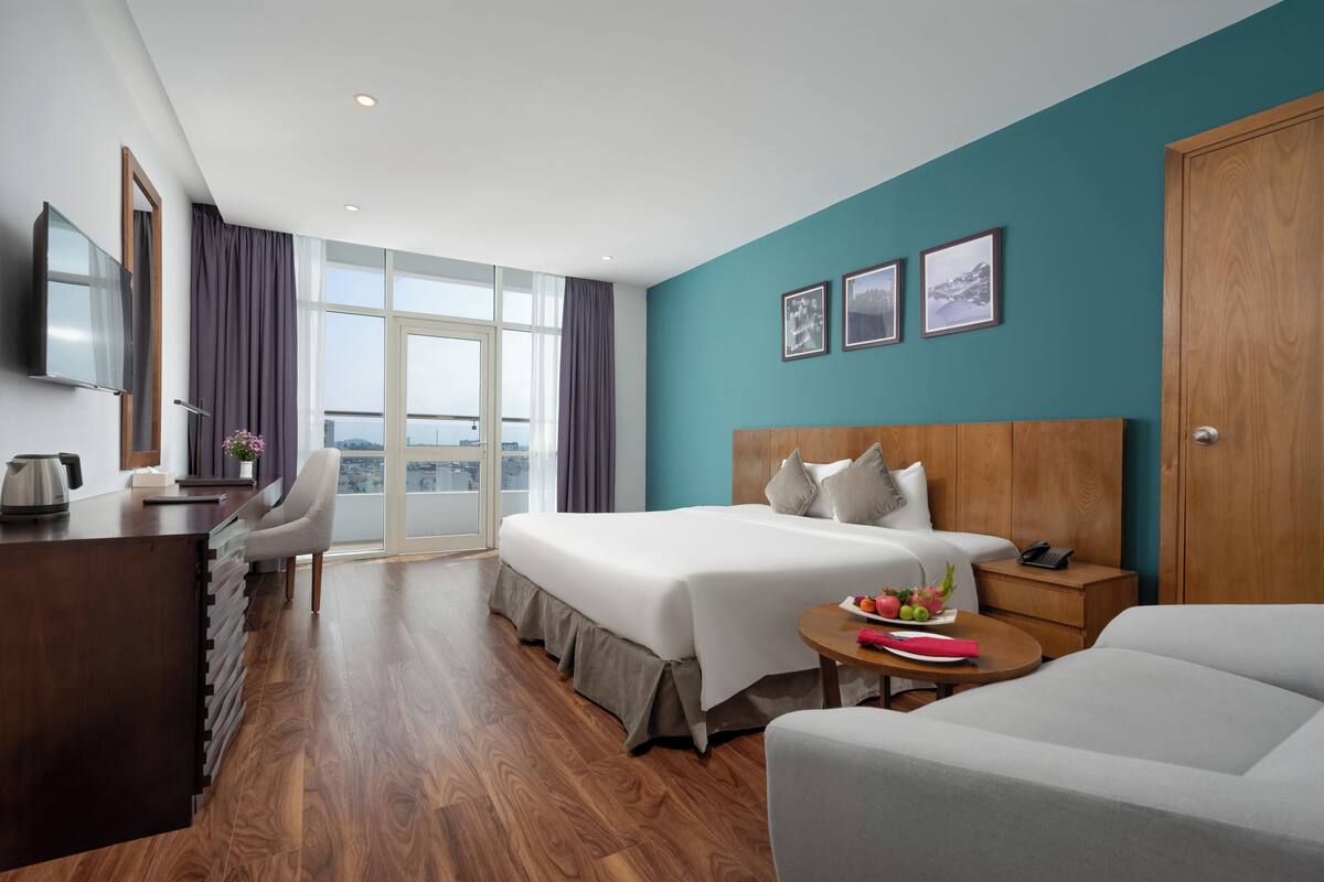 Habitación de hotel con cama, escritorio, silla, mesita de noche con teléfono y vista a la ciudad.