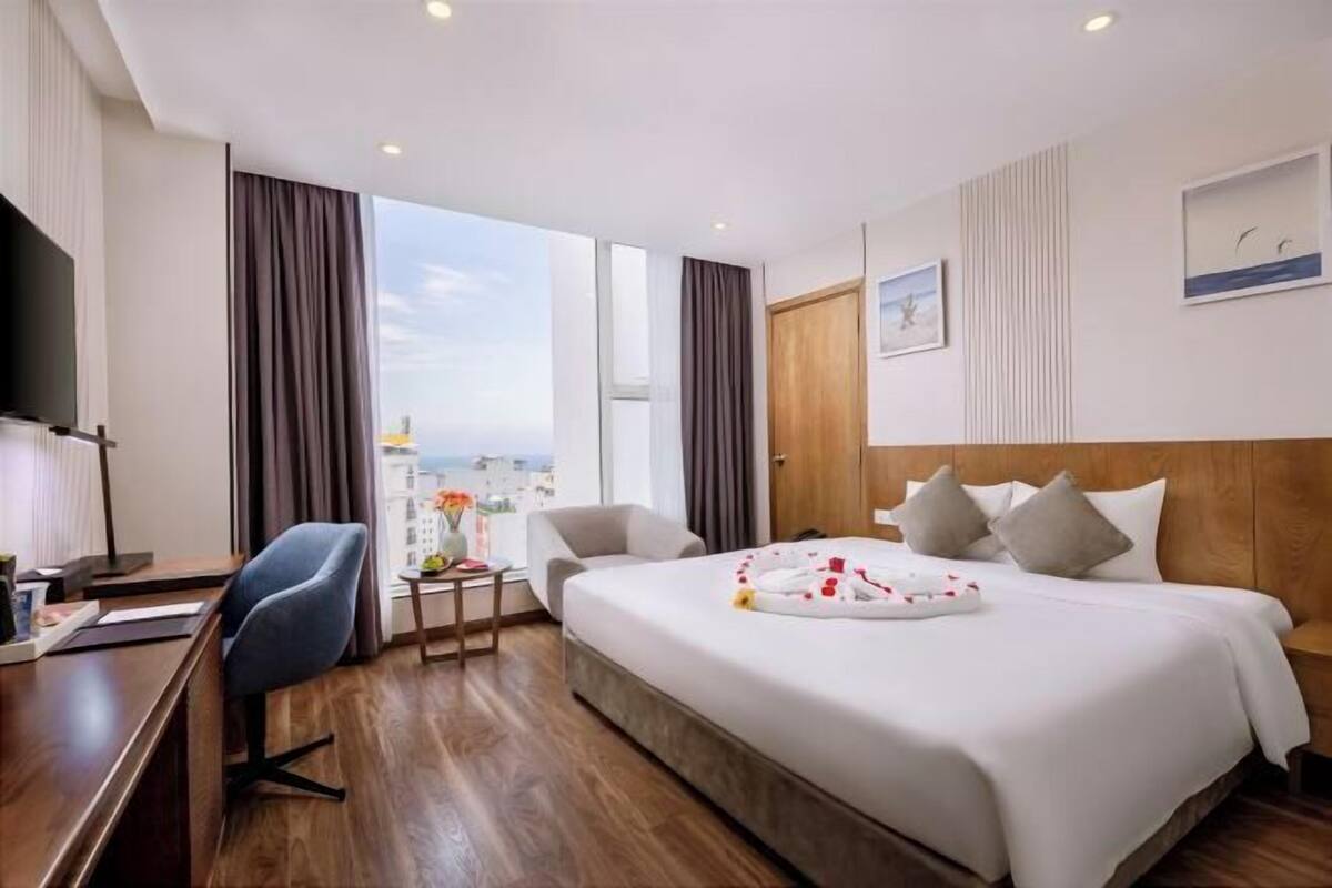 Habitación de hotel con una cama grande, un escritorio, una silla, un televisor y una ventana con vista a la ciudad.