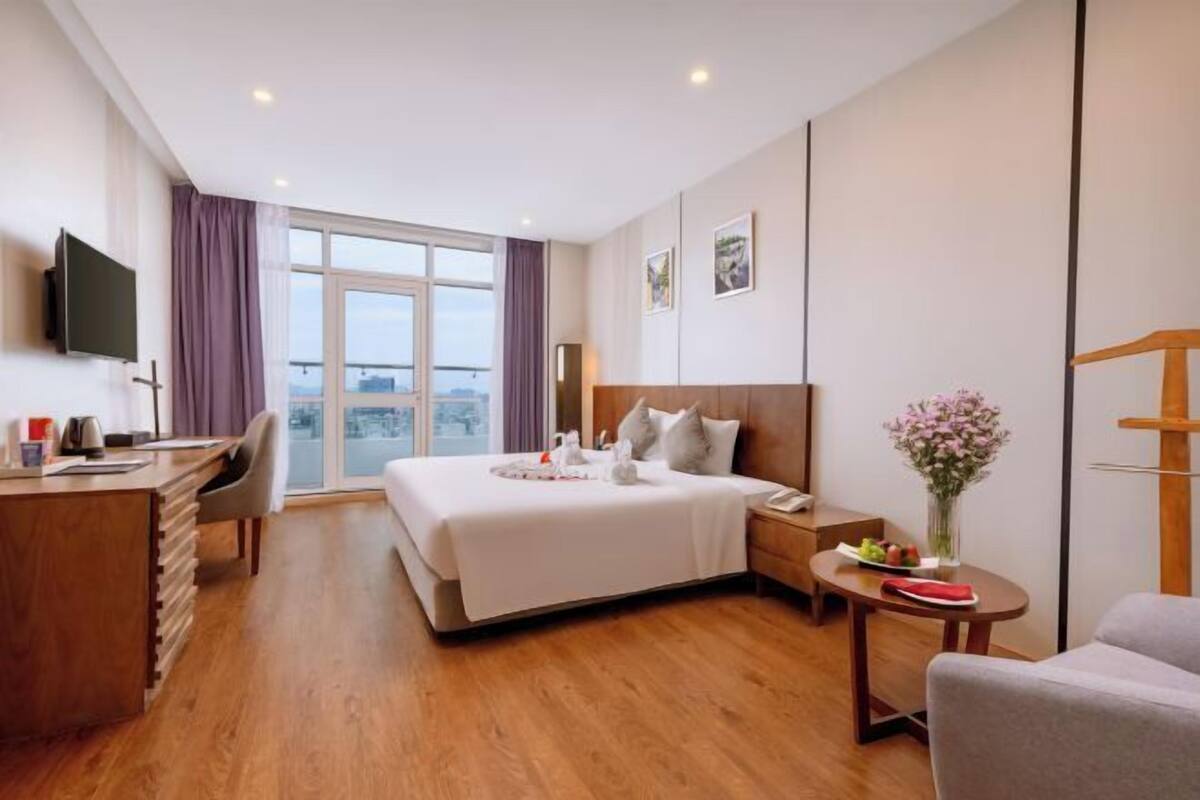 Habitación de hotel con cama, escritorio, silla, televisión y vistas a la ciudad.