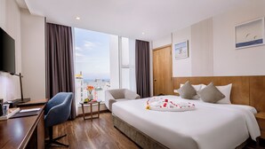 Ein Hotelzimmer mit einem großen Bett, einem Schreibtisch, einem Sessel, einem Fernseher und Blick auf die Stadt.