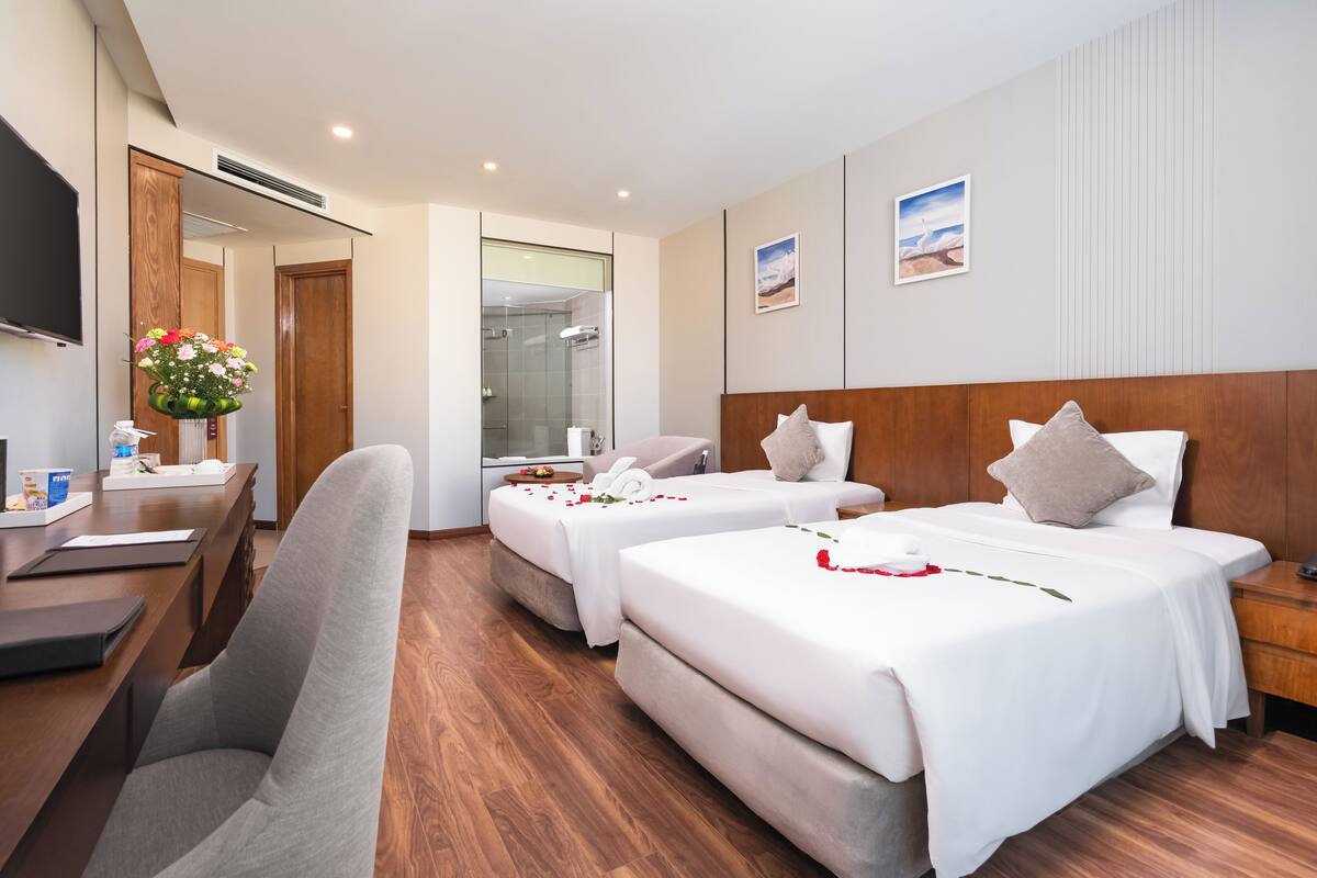 Habitación de hotel con dos camas, un escritorio, una silla, un televisor y zona de ducha.
