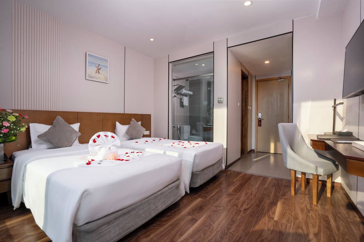 Habitación de hotel con dos camas, un escritorio, una silla, ducha y televisión.