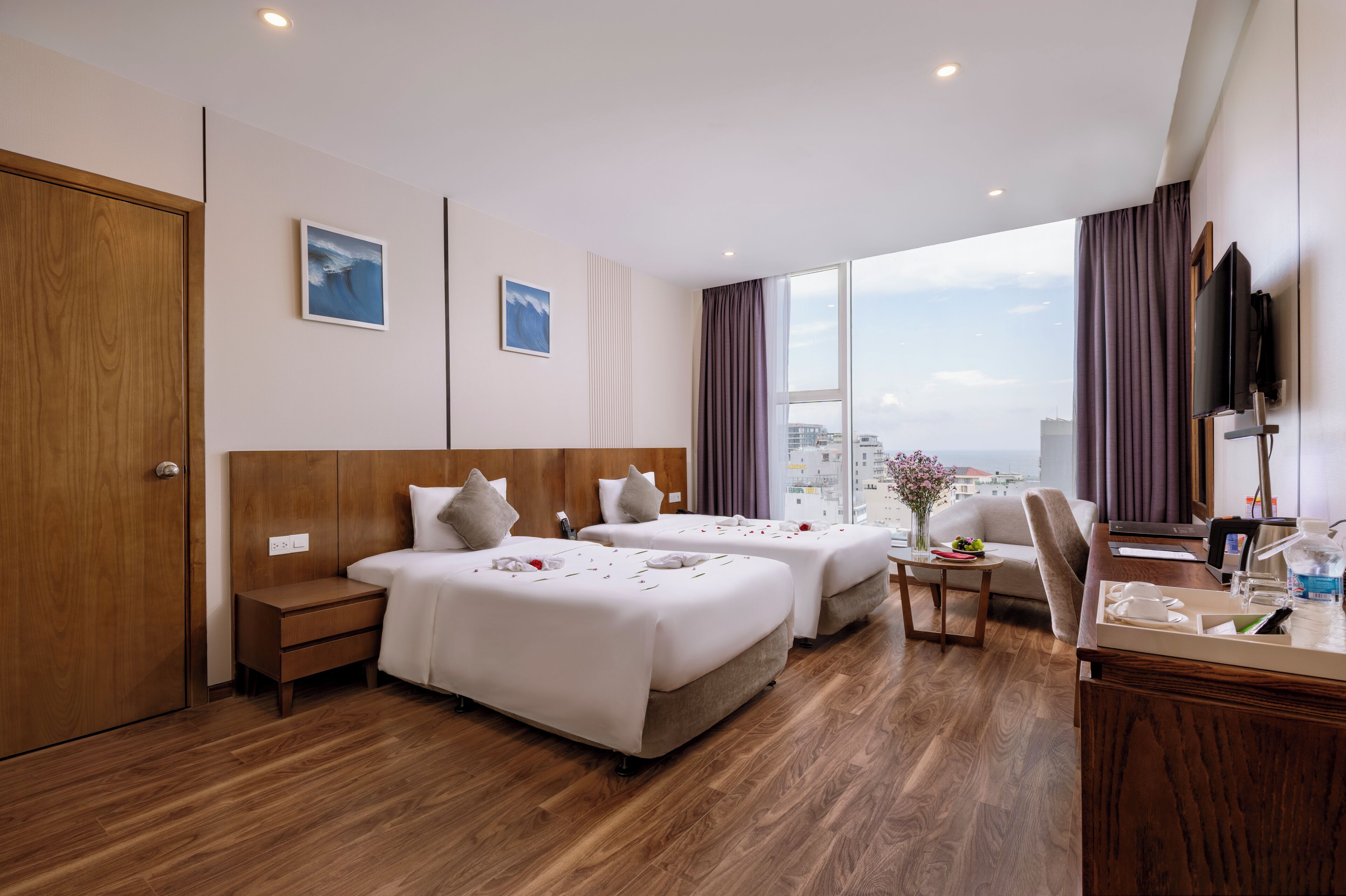 Une chambre d’hôtel avec deux lits, un bureau, une chaise, une télévision et une grande fenêtre donnant sur la ville.