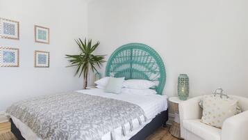Une chambre à coucher avec un lit, une chaise blanche, une plante en pot et des œuvres d’art mural.