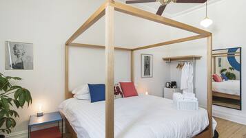Ein Bett mit Baldachin, ausgestattet mit weißer Bettwäsche, ein Nachttisch mit Lampe, ein Spiegel und eine Pflanze.