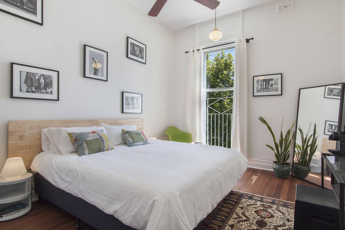 A bedroom with a large bed, a nightstand, a green chair, and several framed pictures on the wall.