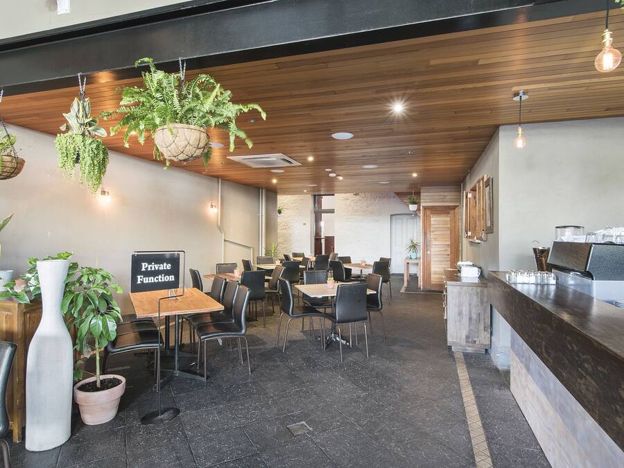 Un café moderno con techo de madera, plantas colgantes y un letrero que dice 'Private Function'.