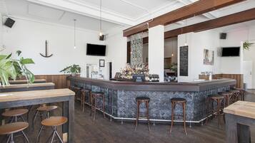 Een bar met een houten toonbank, barstoelen en diverse flessen.