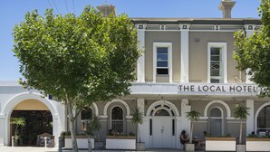 A two-story building with a sign reading "The Local Hotel." It features a large arched entrance, multiple windows, and outdoor seating areas with potted plants. - The Local Hotel (South Fremantle)