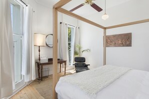 A bedroom with a bed, a desk, a chair, a lamp, and a ceiling fan.