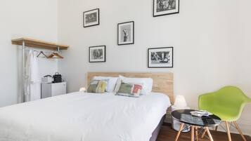 Habitació d'hotel amb un llit, un panell de fusta al capçal, una cadira verda, una taula petita amb una làmpada i diverses fotografies emmarcades a la paret.