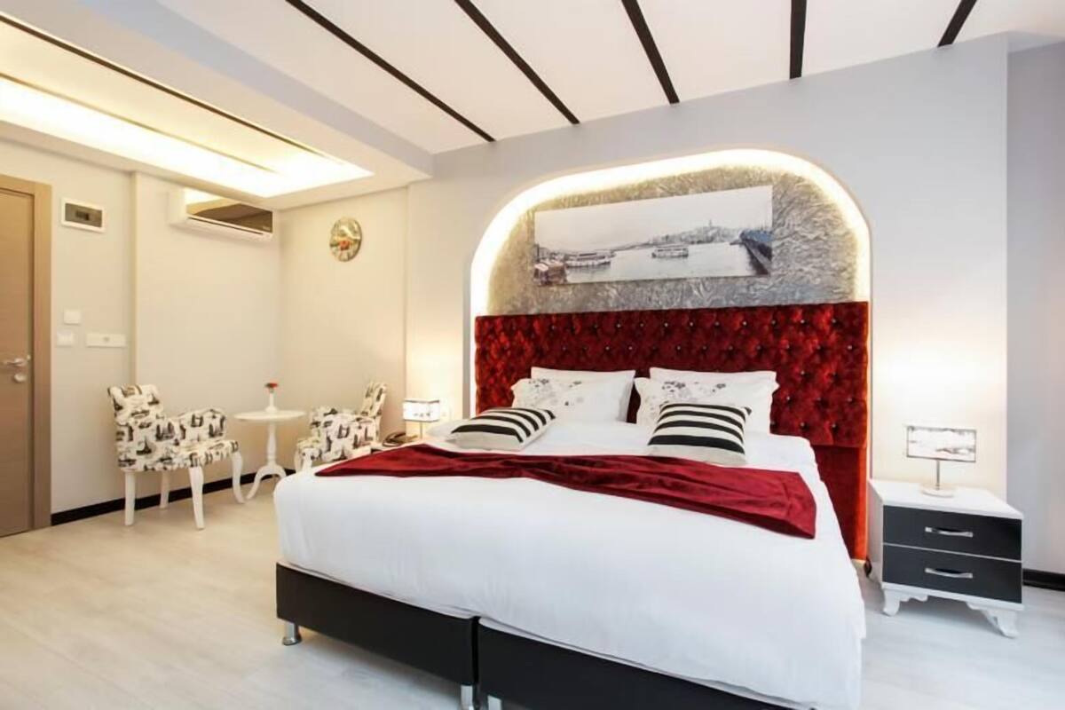 A modern bedroom with a large bed, a red upholstered headboard, a small bedside table, and a chair.