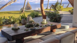 An outdoor dining area with a view of the sea, a hanging chair, and a wooden table set for a meal. - Nay Palad Hideaway (General Luna)