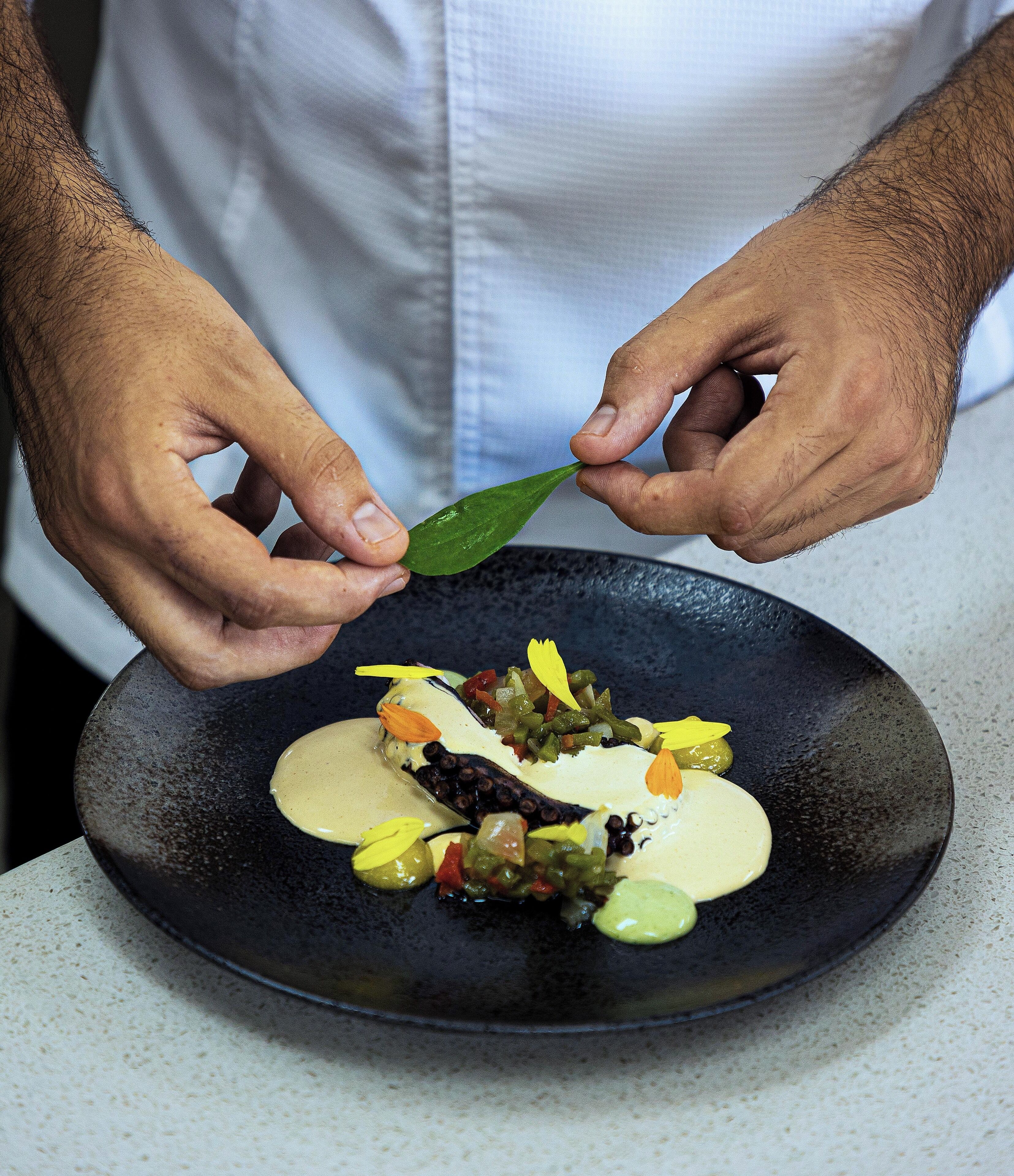 Una persona colocando una hoja verde sobre un plato con comida.