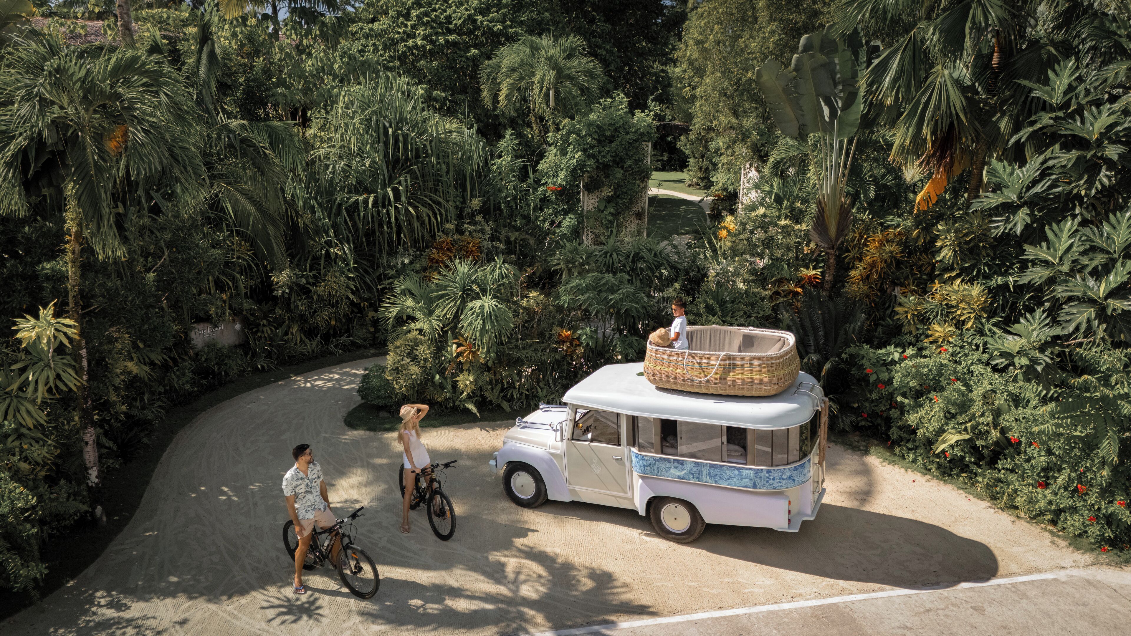 A white van parked on a sandy path surrounded by dense tropical vegetation.