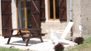 A rustic building with wooden shutters, a picnic table, and a white chair outside. - Château Latour (Fours)