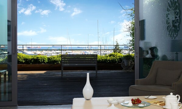 A balcony with a view of the sea, a white vase, and a table with breakfast items.