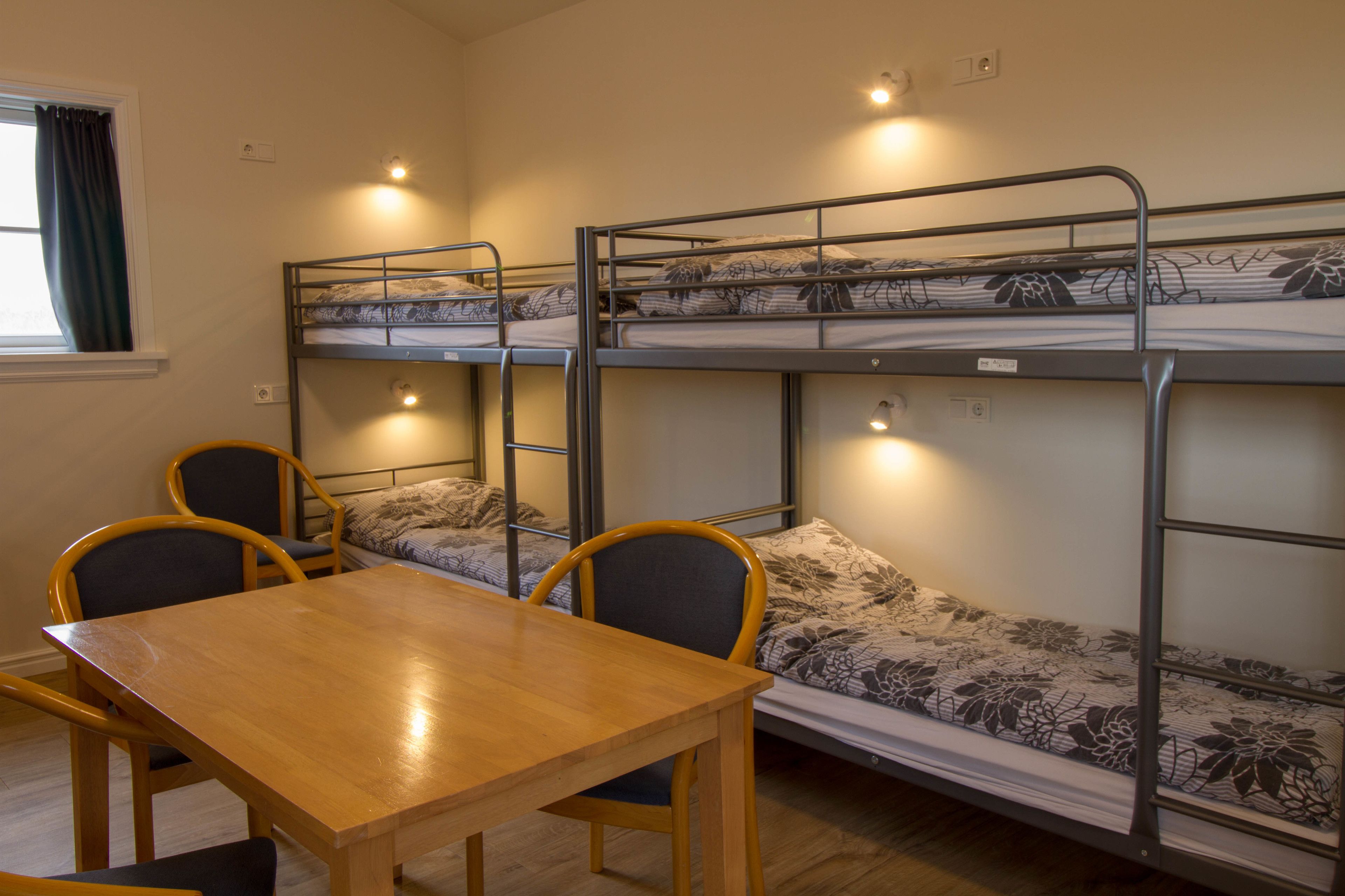 A dormitory room with bunk beds, a wooden table, and two chairs.