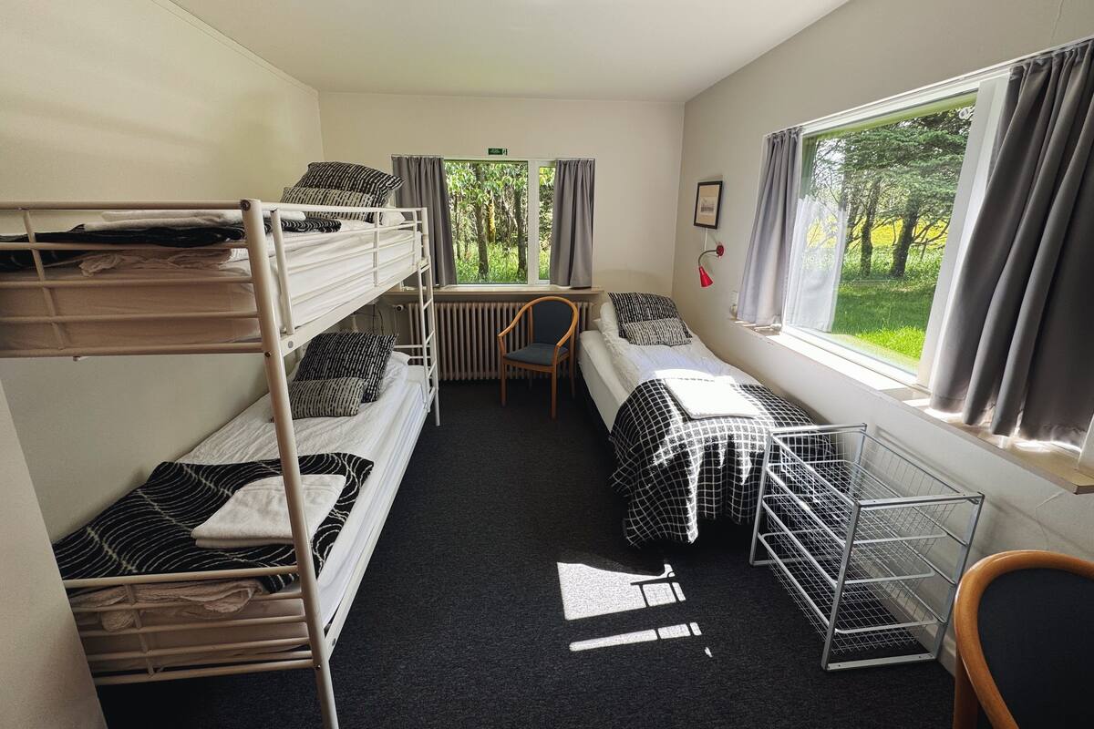 Une chambre de dortoir avec des lits superposés, un bureau, une chaise et une fenêtre avec des rideaux.