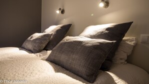 Een net opgemaakt bed met twee kussens en een deken, een wandlamp en een stopcontact aan de muur.