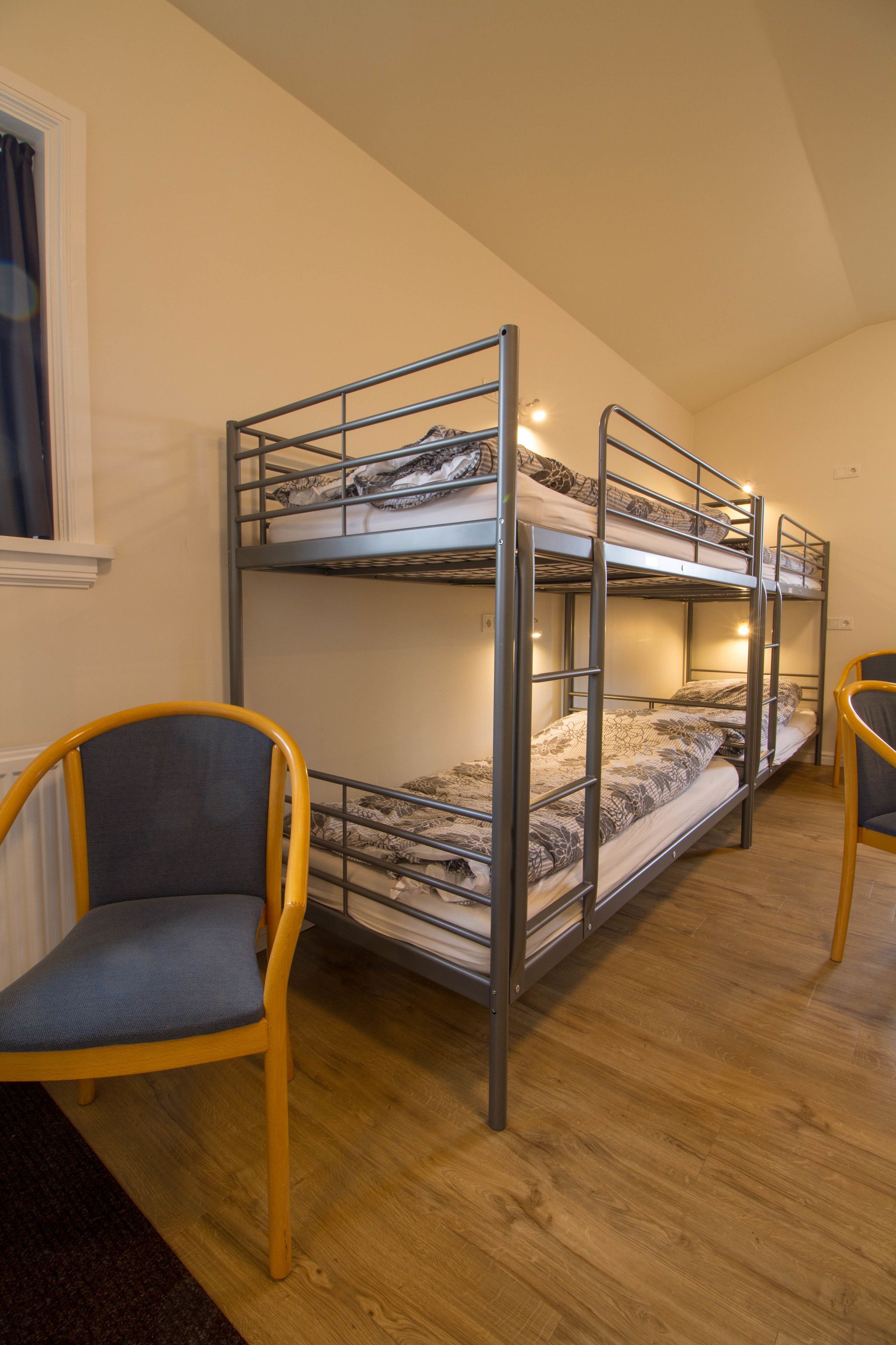 A bunk bed room with a window, a chair, and a wooden floor.